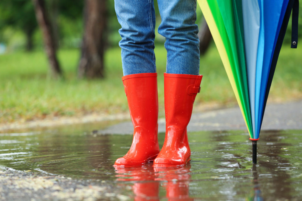 Woman with umbrella and rubber boots in puddle, closeup. Rainy weather