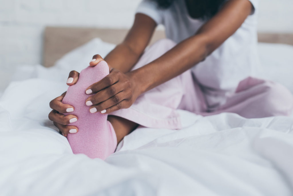 cropped view of african american woman suffering from foot pain in bedroom